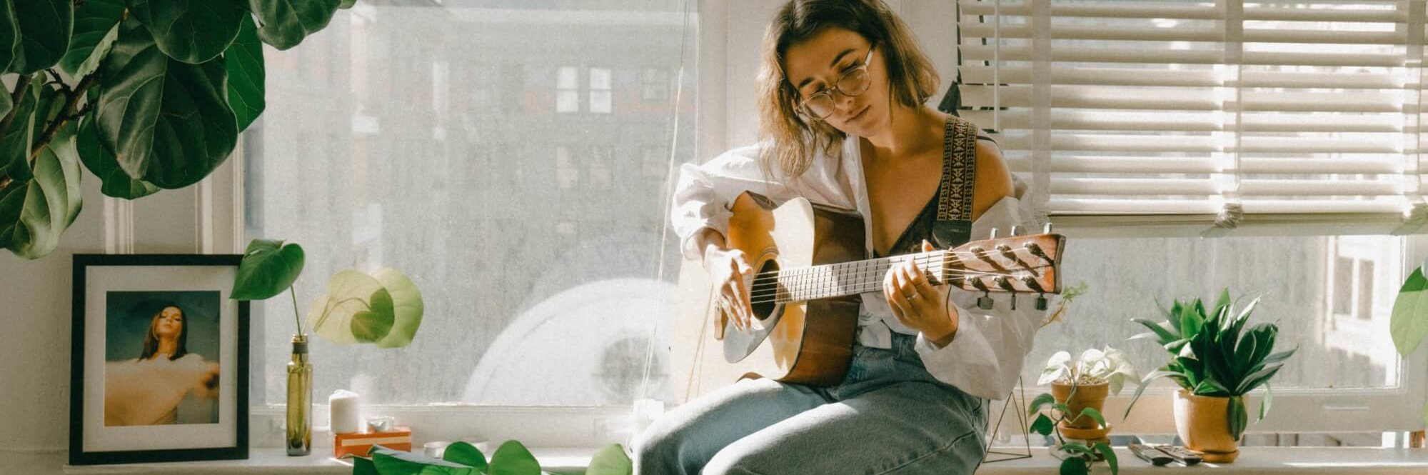 Eine Musikerin spielt Gitarre am Fenster. Viele Künstler:innen nutzen TikTok, um ihre Musik zu vermarkten.