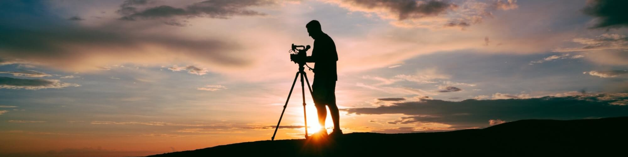 Ein Mensch steht im Sonnenaufgang hinter einer Videokamera. Verschiedene Websites bieten kostenlose Stockvideos an.